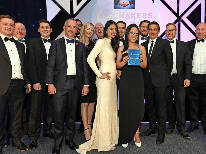 A group of eleven individuals at the Central and East Dealmakers event, dressed in formal evening wear, celebrating with an award plaque.